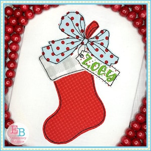 May include: A red Christmas stocking with a black outline, a light blue polka dot bow, and a tag that says "Zoey" in green. The stocking has a plaid cuff and a red patterned body. The image is surrounded by red berries.