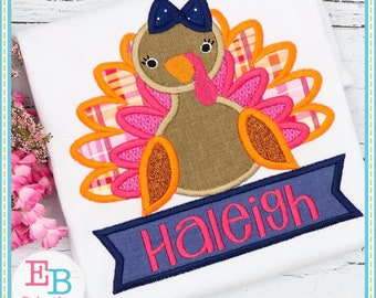 Puede incluir: Diseño bordado de un pavo marrón con plumas rosas y naranjas, un lazo azul y una pancarta azul con el nombre "Haleigh" en letras rosas.