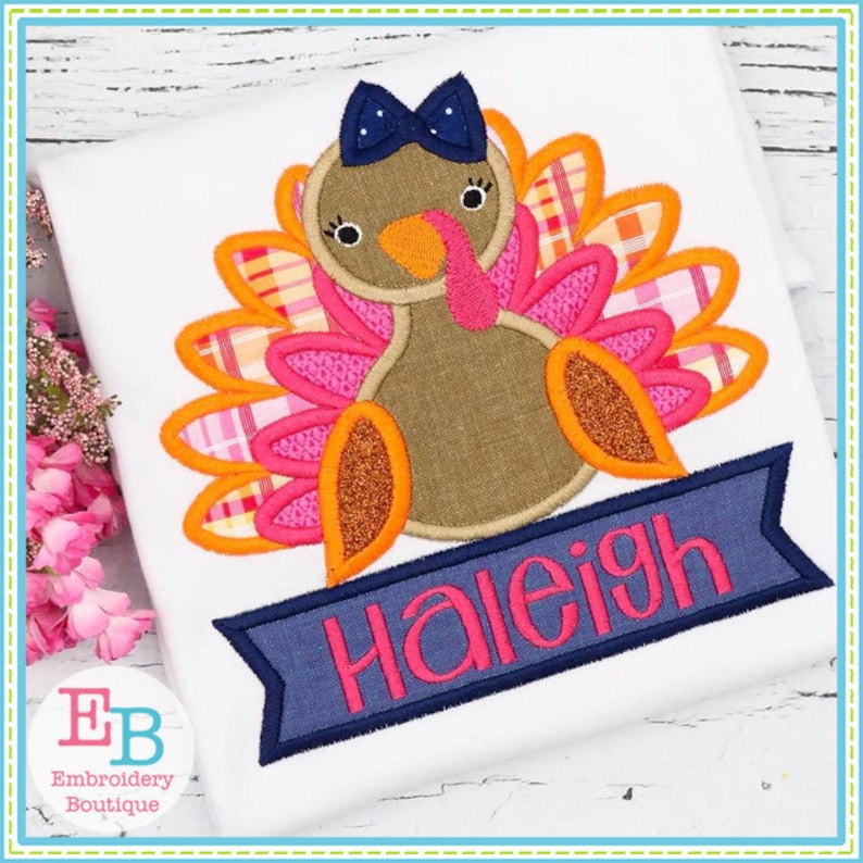 May include: Embroidered design of a brown turkey with pink and orange feathers, a blue bow, and a blue banner with the name "Haleigh" in pink lettering.