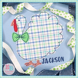 May include: A light blue onesie featuring a plaid turkey applique with a green bow tie and red wattle. The name "JACKSON" is embroidered below the turkey. White and green polka dot ribbon and denim trim frame the onesie.