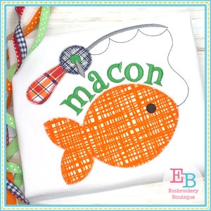 May include: Embroidered design of a fish with a fishing rod and the name "macon" in green letters. The fish is orange with a black eye and a plaid pattern. The fishing rod is gray with a blue and red plaid handle.
