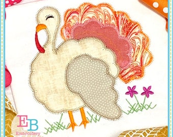 Puede incluir: Diseño de bordado de aplique de un pavo blanco con plumas de cola rosa y naranja, de pie sobre hierba verde con dos flores rosas. El diseño es perfecto para manualidades de Acción de Gracias.
