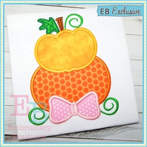 May include: Embroidered design of a stacked pumpkin with a pink polka dot bow. The design is on a white fabric background. The text "EB Exclusive" is in the top right corner of the image.