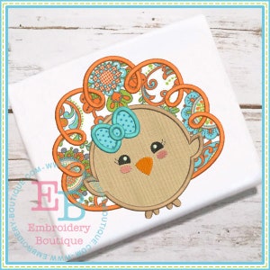May include: Embroidered design of a brown turkey with a blue bow and orange and blue floral pattern around the head.