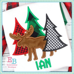 May include: Embroidered design featuring a brown moose standing in front of three Christmas trees. The trees are decorated with red and black buffalo plaid, green and black buffalo plaid, and black and white gingham. The name "IAN" is embroidered in green below the moose.
