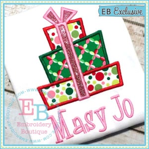 May include: A pink and green embroidered design of a stack of presents with a pink bow on top. The design is on a white t-shirt with the name "Masy Jo" embroidered in pink below the presents. The text "EB Exclusive" is in the top right corner of the image.