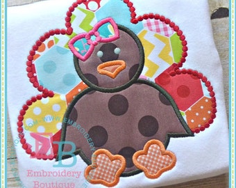May include: A brown turkey with a pink bow and a patchwork tail. The turkey is embroidered on a white fabric.