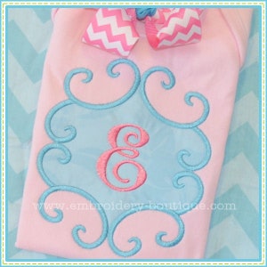 May include: A pink baby onesie with a blue and white swirl design and the letter "E" embroidered in pink in the centre. The onesie has a pink and white chevron bow on the top.
