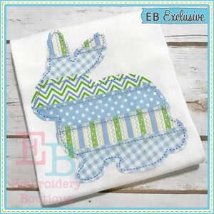 May include: A blue and green patchwork bunny applique design on a white t-shirt. The design is made up of different patterns, including gingham, stripes, polka dots, and zigzags. The text "EB Exclusive" is in the top right corner of the image.