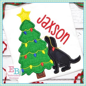 May include: Embroidered design of a black dog pulling on a string of Christmas lights on a green Christmas tree with a yellow star on top. The name "Jackson" is embroidered in red above the dog.