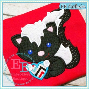 May include: Embroidered design of a black and white skunk holding a blue and red heart. The design is on a red fabric background. The text "EB Exclusive" is in the top right corner of the image.