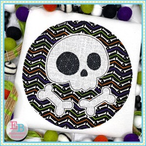 May include: A white skull with crossbones is centered on a black and white chevron pattern circle. The skull has black eyes with a spiderweb design inside each eye. The background is white.