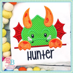 May include: Green and orange embroidered applique of a crying dragon peeking over a sign with the name Hunter.