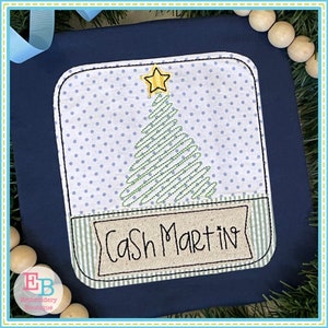 Könnte beinhalten: Ein blauer Stoff mit einem gestickten Weihnachtsbaum in Weiß und Grün mit einem gelben Stern oben. Der Baum befindet sich in einem weißen Quadrat mit einem weißen Punktmuster. Unter dem Baum befindet sich ein Banner mit dem Text "Cash Martin" in Schwarz.