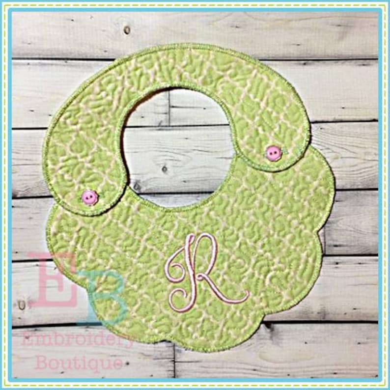May include: A light green quilted baby bib with a floral pattern and a pink embroidered letter "R". The bib has a scalloped edge and two pink buttons. The words "Embroidery Boutique" are at the bottom.