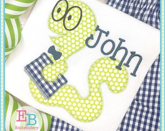 May include: A white onesie with a green, polka-dotted, cartoon worm wearing a blue bow tie and holding a blue and white checkered gift box. The name "John" is embroidered in blue on the onesie.