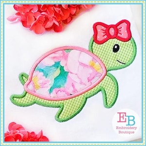 May include: Green and pink applique of a turtle with a pink bow. The turtle's shell has a floral pattern.