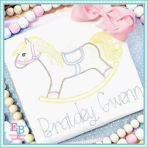 May include: A white onesie with a yellow rocking horse embroidery design and the name "Braidey Gwenn" embroidered in cursive script.