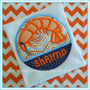 May include: A blue and white circle with a shrimp design and the word "shrimp" in orange letters. The circle is on a white fabric with an orange and white chevron pattern.