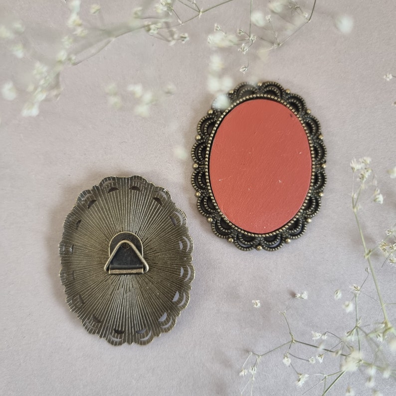 May include: Two ornate metal frames, one with a red backing and the other with a decorative back. Both frames have a scalloped edge and a hanging loop.