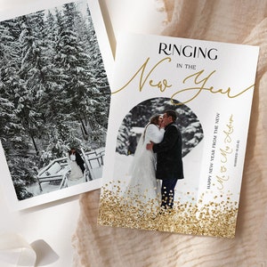 Pode incluir: Um cartão branco com glitter dourado e uma foto de um casal se beijando em uma floresta nevada. O texto no cartão diz "Ringing in the New Year" e "Happy New Year from the new Mr. & Mrs. Adams" com a data "Married 01.23.45".