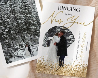 May include: A white card with gold glitter and a photo of a couple kissing in a snowy forest. The text on the card reads "Ringing in the New Year" and "Happy New Year from the new Mr. & Mrs. Adams" with the date "Married 01.23.45".
