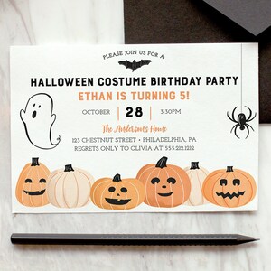 以下が含まれることがあります： ハロウィーンのコスチューム誕生日パーティーの招待状。お化け、クモ、カボチャが描かれています。招待状には「イーサンは5歳！」と書かれており、日付、時間、住所も記載されています。黒い封筒と鉛筆も画像にあります。