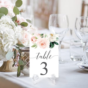 Puede incluir: Tarjeta de número de mesa blanca con diseño floral rosa y blanco. La tarjeta dice "mesa 3" en letra cursiva gris.