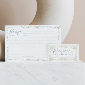 Könnte beinhalten: Zwei weiße Rezeptkarten mit floralen Verzierungen. Die größere Karte trägt das Wort "Recipe" in Schreibschrift und Felder für Zutaten und Anweisungen. Die kleinere Karte lautet "Recipe for the Bride-to-Be".