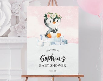 May include: A baby shower sign on a wooden easel. The sign features a watercolor illustration of a penguin wearing a floral crown, sitting on ice. The sign reads "Welcome to Sophia's Baby Shower" with the date 01.23.45. Pink balloons are in the background.