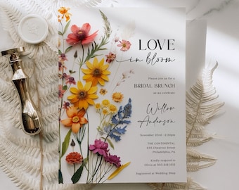 May include: A floral bridal brunch invitation with a white background and a colourful pressed flower design. The text reads "LOVE in bloom" and includes the bride's name, Willow Anderson, the date and time of the event, and the location. The invitation also includes the text "Kindly respond to Olivia at 555.212.1212. Registered at Wedding Shop."