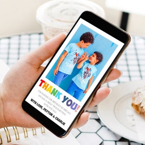 May include: A smartphone displays a digital card with the words "THANK YOU!" in rainbow colors. The card features a photo of two boys in blue shirts and pants. Text below reads "FOR MAKING OUR BIRTHDAY SO SPECIAL!" and "WITH LOVE, PEYTON & CHARLIE."