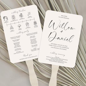 May include: Two cream-colored wedding fans with text and illustrations. One fan displays a wedding timeline and party details. The other fan says "Willow + Daniel" with the wedding date and location. The fans have a simple, elegant design.