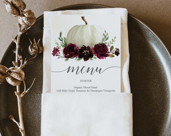 Puede incluir: Una calabaza blanca con hojas verdes y flores burdeos está en una tarjeta de menú blanca con la palabra "menú" en cursiva. El texto debajo dice "Starter Organic Mixed Salad with Baby Grape Tomatoes & Champagne Vinaigrette".