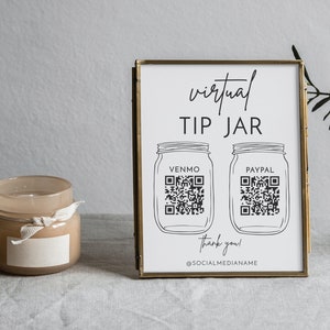 May include: A white sign with black text and illustrations in a gold frame. The sign reads "virtual tip jar" with two mason jar illustrations. Each jar has a QR code and the text "Venmo" and "Paypal". The sign also includes the text "thank you!" and "@socialmedianamae".