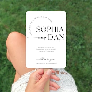May include: White wedding fan with black text that reads "Welcome to the best day ever Sophia and Dan" with the date and time of the wedding and the location. The text also says "Thank you for being a part of our special day!"