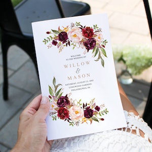 May include: A wedding invitation featuring a floral design in shades of burgundy, pink, and green. The text reads "Welcome to the wedding of Willow & Mason, Saturday, August 23, 2045, Longwood Gardens, Philadelphia, PA".