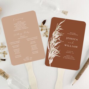 May include: Two wedding ceremony fans. The first fan is peach colored with the wedding ceremony order of events printed on it. The second fan is brown with a watercolor illustration of a dried grass plant. The text on the fan reads "Welcome to our beginning Jessica and William 01.23.45 Sedona, AZ Thank you for being a part of our special day!"
