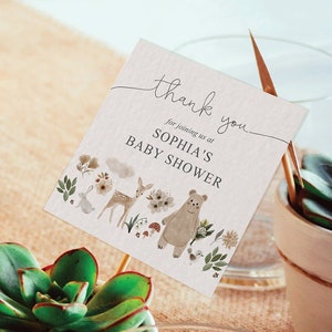 Op de afbeelding: Een kleine witte pot met een vetplant erin. Een bedankkaart met een bosmotief is aan de pot bevestigd. De kaart zegt "Bedankt voor je komst naar Sophia's babyshower".