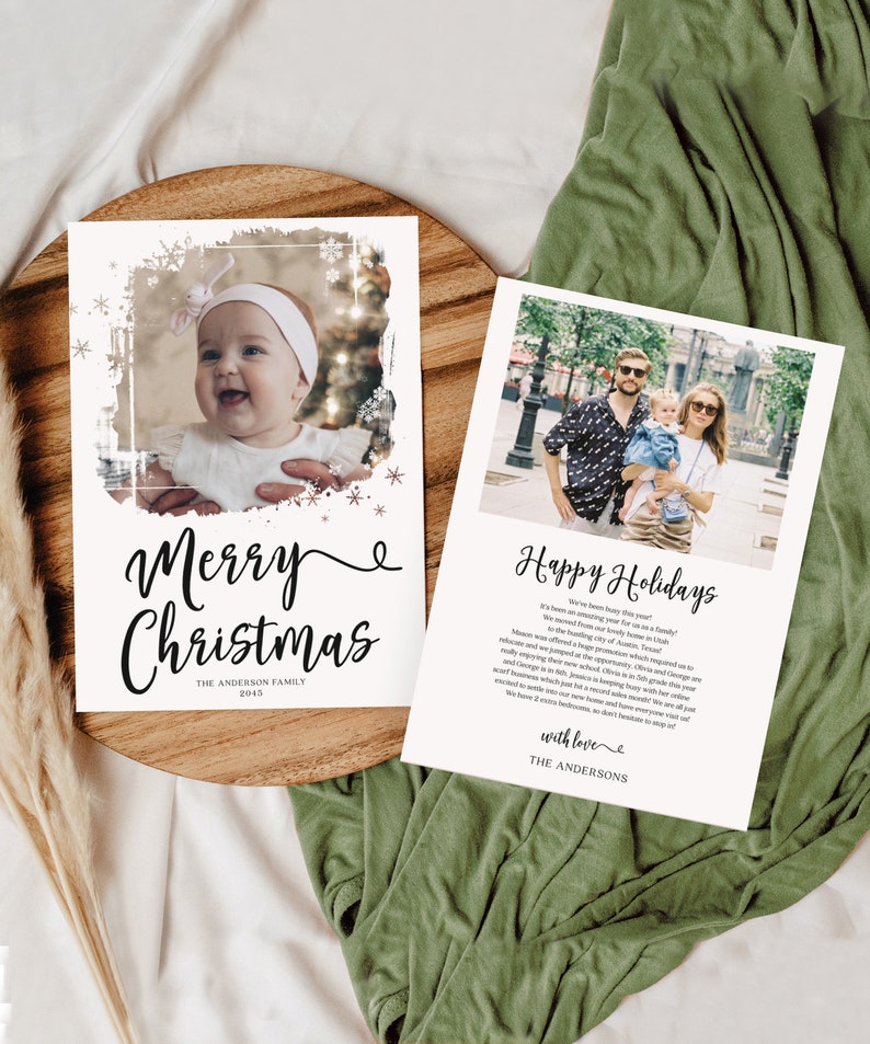 May include: Two holiday cards with family photos. One card says "Merry Christmas" with a baby photo and snowflakes. The other says "Happy Holidays" with a family photo. Both cards are on a wooden tray.