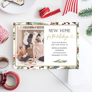 May include: A holiday-themed card with a photo of a family in front of a fireplace. The card features the text "NEW HOME for the holidays" in black and gold, along with address details. Decorative elements include greenery and berries.