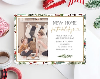May include: A holiday-themed card with a photo of a family in front of a fireplace. The card features the text "NEW HOME for the holidays" in black and gold, along with address details. Decorative elements include greenery and berries.