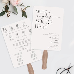May include: Two wedding fans with wooden handles. One fan displays a wedding timeline with illustrations. The other fan says "We're so glad you're here" and wedding details. A pair of scissors and flowers are in the background.