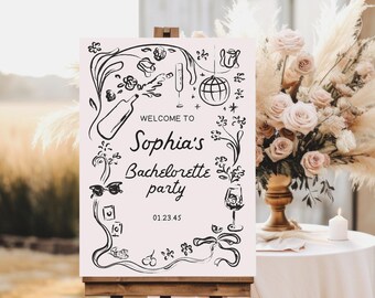 May include: A white sign with black ink drawings of party items like champagne glasses, a disco ball, and cherries. The text on the sign reads "Welcome to Sophia's Bachelorette party 012345". The sign is on a wooden easel.