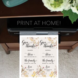 May include: A printer is shown with two printed cards. The cards read "Give Thanks" with floral accents and the text "bless the food before us, the family beside us, and the love between us, amen." The text "Print at Home!" is above the printer.