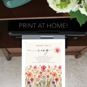 May include: A printable card with a floral background and the text "Please take a ring and hold it tight. Try not to say "bride" or "wedding" with all of your might. If you hear someone say it, snatch up their ring. To win at the end, collect the most bling."