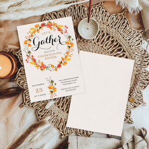 K&ouml;nnte beinhalten: Einladung zum Thanksgiving-Dinner mit dem Text "Let's Gather" in eleganter Schrift, umgeben von einem Kranz aus Herbstbl&auml;ttern und Beeren. Die Einladung enth&auml;lt Datum, Uhrzeit und Ort. Eine leere Karte liegt daneben.