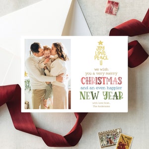 May include: A rectangular holiday greeting card featuring a photograph of a family of three embracing on the left side. The right side displays gold text reading JOY LOVE PEACE, followed by we wish you a very merry CHRISTMAS and an even happier NEW YEAR with love from, The Andersons.