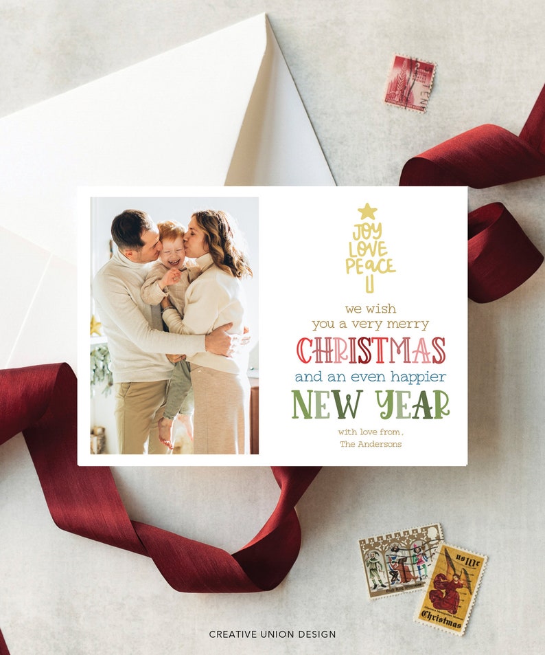 May include: A rectangular holiday greeting card featuring a photograph of a family of three embracing on the left side. The right side displays gold text reading JOY LOVE PEACE, followed by we wish you a very merry CHRISTMAS and an even happier NEW YEAR with love from, The Andersons.