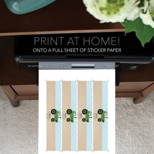 May include: A printer is printing a sheet of paper with a design featuring green tractors, blue stripes, and the text "PRINT AT HOME!" and "ONTO A FULL SHEET OF STICKER PAPER." The design also includes the text "Monk's" and "Noah's."
